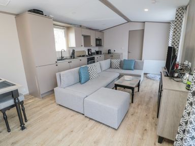 A living room with a gray sectional sofa and a small coffee table next to a kitchen with beige cabinets and appliances at Dreams & Streams in Bockenfield Country Park near West Thirston