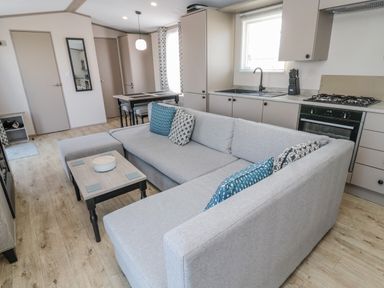 A living room with a grey sectional sofa and a wooden coffee table adjacent to a kitchen with beige cabinets and a dining table at Dreams & Streams Bockenfield Country Park near West Thirston