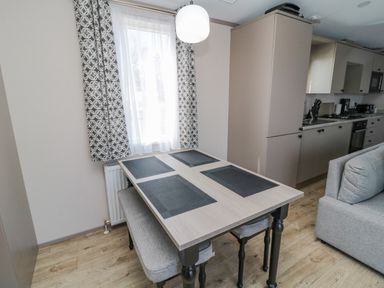A dining table with four place mats and bench seating next to a window with patterned curtains in a kitchen at Dreams & Streams Bockenfield Country Park near West Thirston