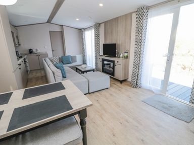 A living area with a sectional sofa blue and patterned cushions a coffee table a dining table with placemats and a TV on a cabinet with a fireplace at Dreams & Streams in Bockenfield Country Park near West Thirston