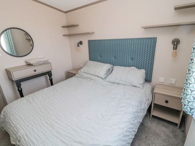 A bedroom with a double bed two side tables wall shelves a round mirror and a window with patterned curtains at Dreams & Streams Bockenfield Country Park near West Thirston