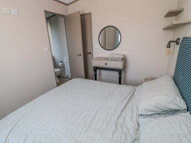 A bedroom with a bed a small table with folded towels a round mirror and an open door showing a bathroom at Dreams & Streams in Bockenfield Country Park near West Thirston