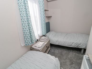 A bedroom with two single beds a nightstand with folded towels patterned curtains and carpet flooring at Dreams & Streams in Bockenfield Country Park near West Thirston