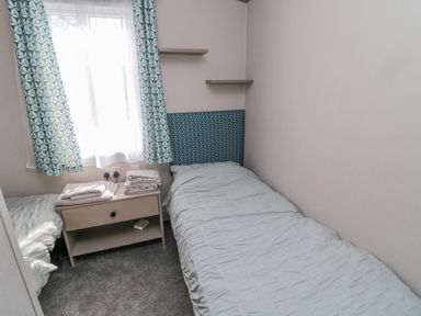 A small bedroom with two single beds a bedside table with folded towels shelves and patterned curtains at Dreams & Streams in Bockenfield Country Park near West Thirston