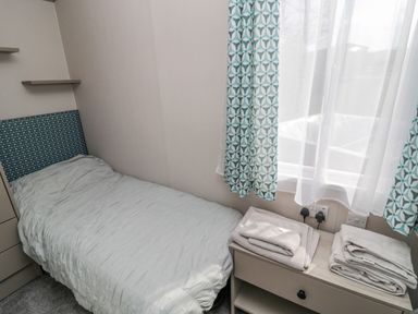 A bedroom with a single bed bedside table with folded towels and patterned curtains at Dreams & Streams Bockenfield Country Park near West Thirston