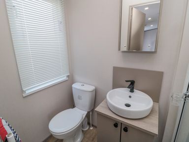 A bathroom with a toilet next to a window and a sink with a mirror above at Dreams & Streams in Bockenfield Country Park near West Thirston