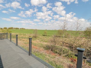 A deck with glass railing overlooking a grassy field and sparse trees at Dreams & Streams in Bockenfield Country Park near West Thirston