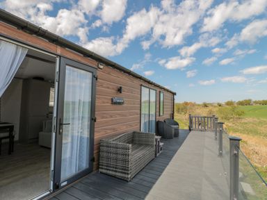 An outdoor deck with wicker furniture attached to a building overlooking a field at Dreams & Streams in Bockenfield Country Park near West Thirston