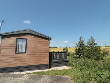 A wooden cabin exterior with a window and a small fenced patio beside greenery at Dreams & Streams Bockenfield Country Park near West Thirston