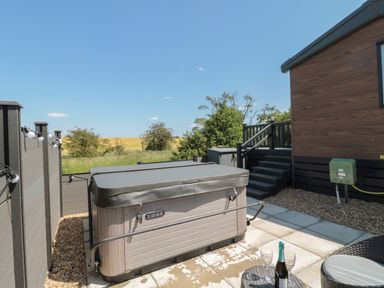 An outdoor patio area with a covered hot tub a round table with wine glasses a bottle and steps leading to a building at Dreams & Streams Bockenfield Country Park near West Thirston