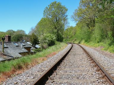 Railway tracks curving through a green area with trees and a house roof visible on the left side at Little Barton in Stogumber near Watchet