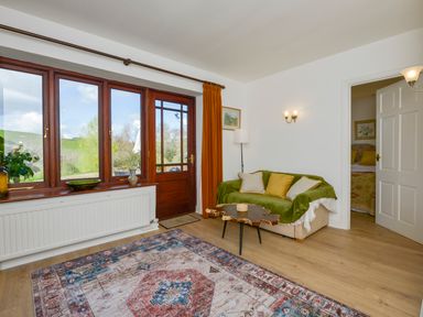 A living room with a sofa green throw wooden coffee table and large windows at Little Barton in Stogumber near Watchet