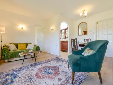 A living room with green sofa, wooden coffee table, blue armchair, dining table, and kitchen visible through an arch at Little Barton Stogumber near Watchet