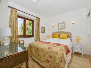 A bedroom with a double bed yellow pillows and floral curtains at Little Barton in Stogumber near Watchet
