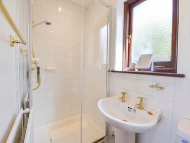 A bathroom with a shower enclosure a white sink with gold taps a frosted window and tiled walls at Little Barton in Stogumber near Watchet