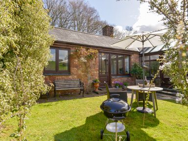 A garden with a stone patio table umbrella chairs a barbecue and a wooden bench outside a stone house at Little Barton Stogumber near Watchet