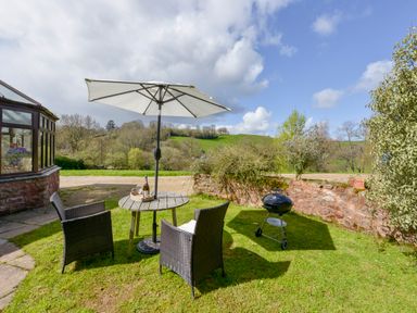 A garden seating area with a table umbrella two chairs and a barbecue grill at Little Barton in Stogumber near Watchet