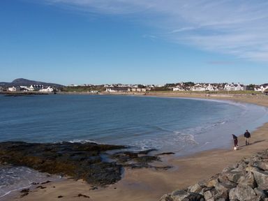 A beach with rocky shoreline and two people walking a dog near water at Beach Reach in Valley