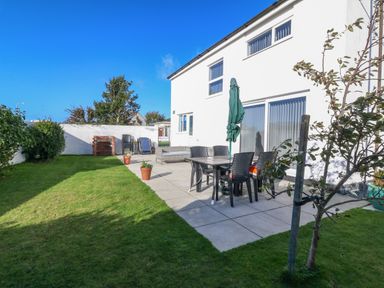 A backyard with a patio table and chairs umbrella and potted plants next to a white house at Beach Reach in Valley
