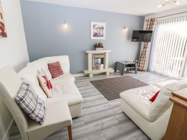 A living room with white sofas a small fireplace a wall mounted tv and vertical blinds at Beach Reach in Valley