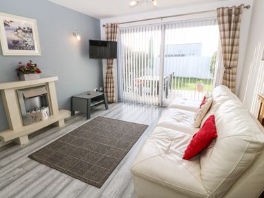 A living room with a white sofa with cushions a gray rug a fireplace a wall mounted tv and sliding glass doors with vertical blinds at Beach Reach in Valley