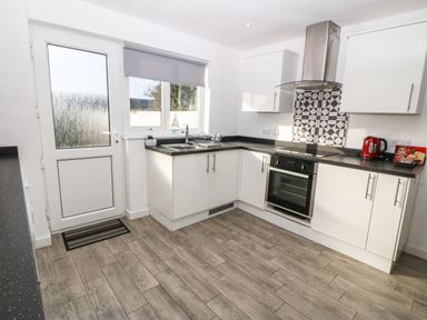 A kitchen with white cabinets a black countertop a built-in oven a red kettle a patterned backsplash a window and a door at Beach Reach in Valley