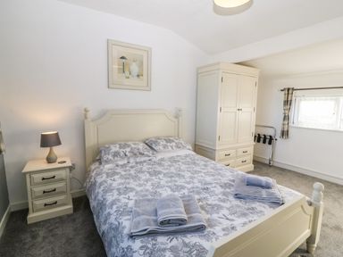 A bedroom with a double bed, bedside table with lamp, wardrobe, window with curtains at Beach Reach in Valley