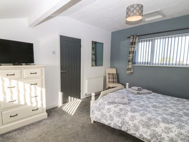 A bedroom with a bed with folded towels a chest of drawers with a television a chair and a window with vertical blinds at Beach Reach in Valley