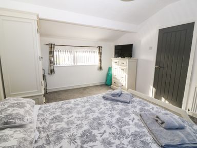A bedroom with a bed, wardrobe, chest of drawers with a TV on top, a window with curtains and a dark door at Beach Reach in Valley