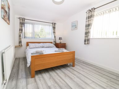 A bedroom with a wooden bed and bedside table with a lamp two windows with vertical blinds and plaid curtains on wooden floor at Beach Reach in Valley