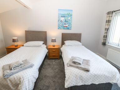 A bedroom with two single beds bedside tables lamps a window with curtains and a painting on the wall at Beach Reach in Valley