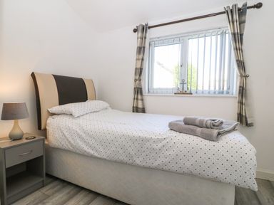 A bedroom with a bed covered in white and black polka dot bedding a bedside table with a lamp and folded towels on the bed at Beach Reach in Valley