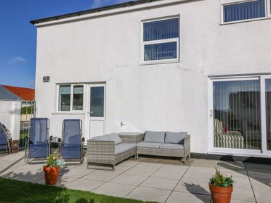 A patio with two blue outdoor chairs and a gray wicker corner sofa set outside a white house at Beach Reach in Valley