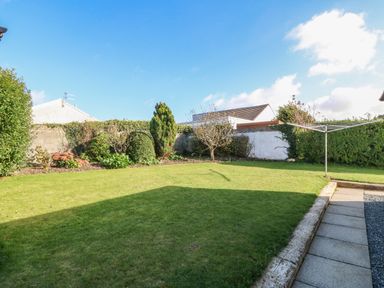 A backyard with a grassy lawn, garden beds with shrubs, a paved walkway, and a rotary clothesline at Beach Reach in Valley