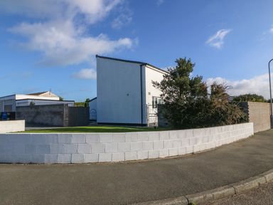 A detached white house with a garden and bushes behind a low white brick wall at Beach Reach in Valley