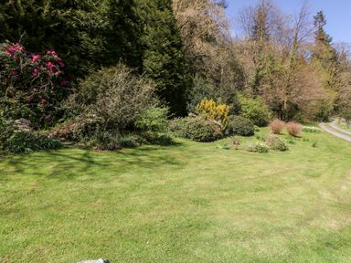 A garden with grass lawn and various shrubs and trees beside a dirt path in Greffyn Betws-Y-Coed