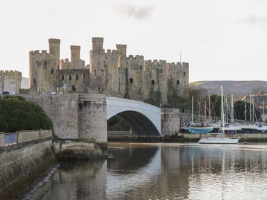 A large stone castle beside a body of water with a white arched bridge and sailboats at Greffyn in Betws-Y-Coed