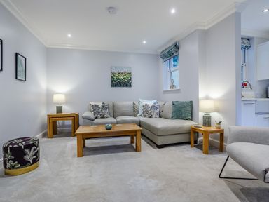A living room with a leather corner sofa wooden tables lamps and artwork at Jasmine Cottage in Mickleton Gloucestershire