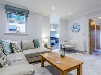 A living room with a beige sofa cushions wooden coffee table and a gray armchair at Jasmine Cottage in Mickleton Gloucestershire
