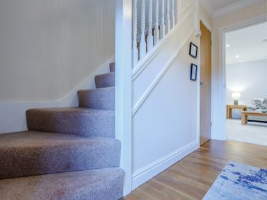A carpeted staircase with wood flooring and a doorway leading to a living room with a sofa and lamp at Jasmine Cottage in Mickleton Gloucestershire