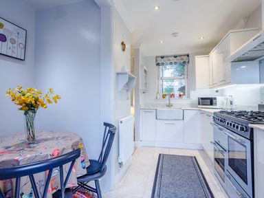 A kitchen with a dining table and chairs a sink stove microwave and window at Jasmine Cottage in Mickleton Gloucestershire