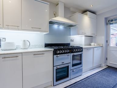 A kitchen with white cabinets a stove toaster kettle and teapot at Jasmine Cottage in Mickleton Gloucestershire