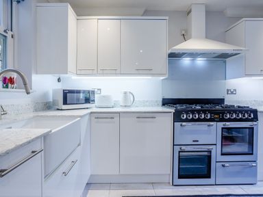 A kitchen with white cabinets a microwave kettle and toaster on the counter and a large stove at Jasmine Cottage in Mickleton Gloucestershire
