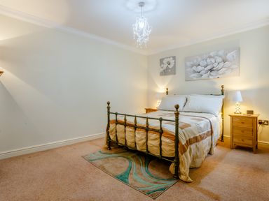 A bedroom with a metal bed frame two bedside tables with lamps and flower paintings on the wall at Jasmine Cottage in Mickleton Gloucestershire
