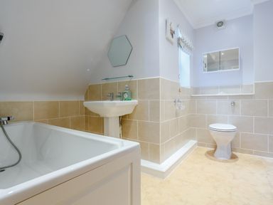 A bathroom with a bathtub sink toilet beige tiled walls and a hexagonal mirror at Jasmine Cottage in Mickleton Gloucestershire
