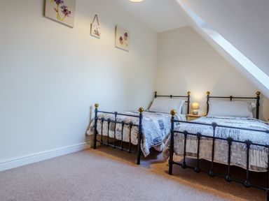 A bedroom with two metal-framed single beds a bedside table with a lamp and artwork on the wall at Jasmine Cottage in Mickleton Gloucestershire