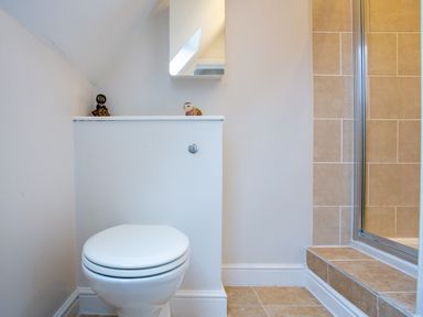A bathroom with a white toilet and a glass shower door with beige tiled walls at Jasmine Cottage in Mickleton Gloucestershire