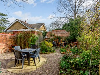 A garden patio with a table and four chairs surrounded by plants and trees at Jasmine Cottage in Mickleton Gloucestershire