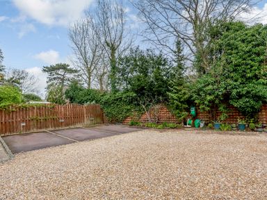 A gravel driveway with parking spaces and a wooden fence surrounded by trees and plants at Jasmine Cottage in Mickleton Gloucestershire