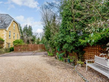 A gravel driveway with a wooden bench and potted plants along a fence and a stone house nearby at Jasmine Cottage in Mickleton Gloucestershire